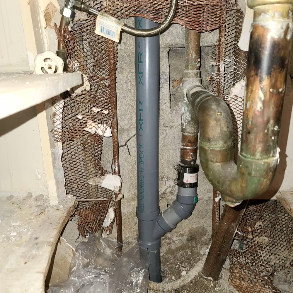An old corroded copper drain beside its new grey PVC replacement